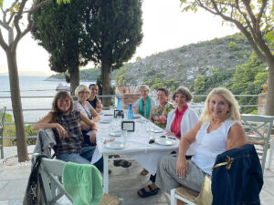 People sitting at a dinning table outside with the mountains and water behind them.